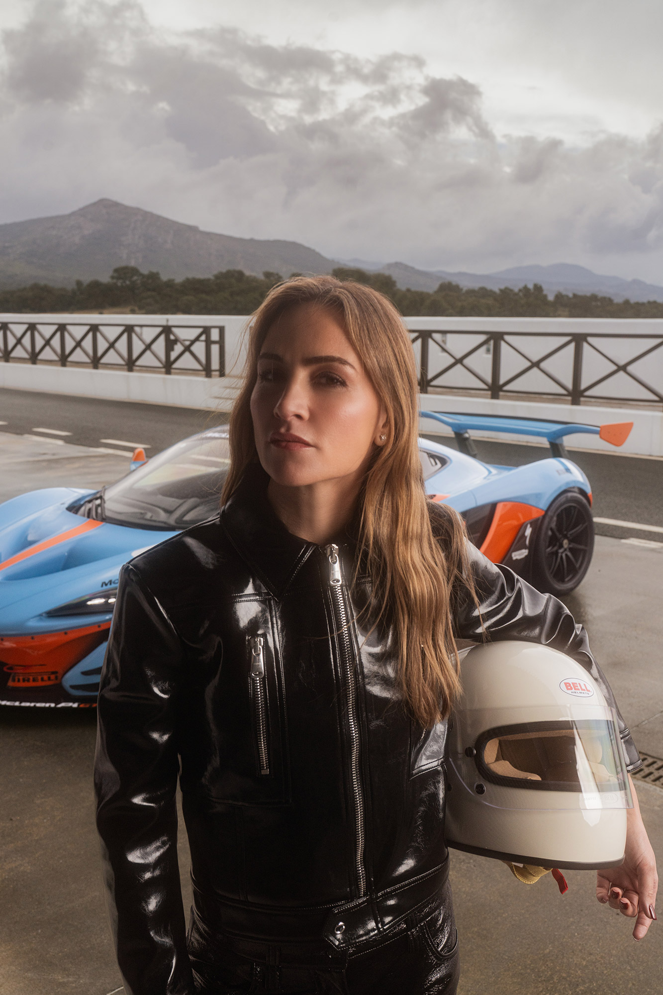 Carmen standing in front of a supercar holding a racing helmet