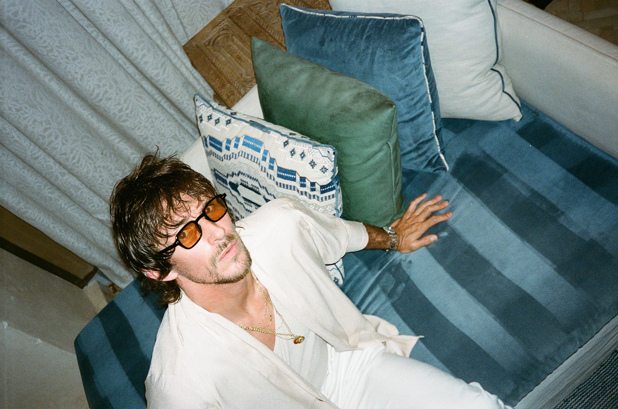 Jake sitting on a sofa in all white clothing with sunglasses on