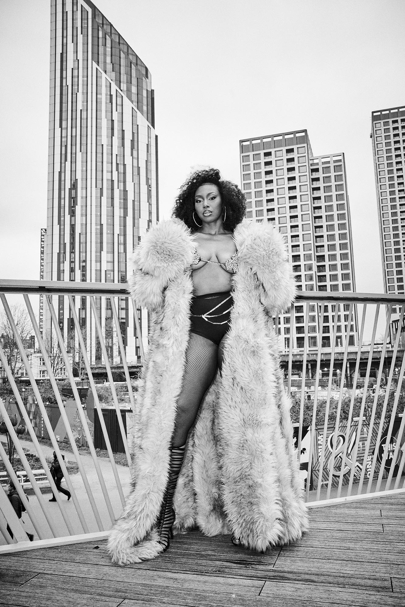 Ms. Banks standing on a bridge in a fur coat