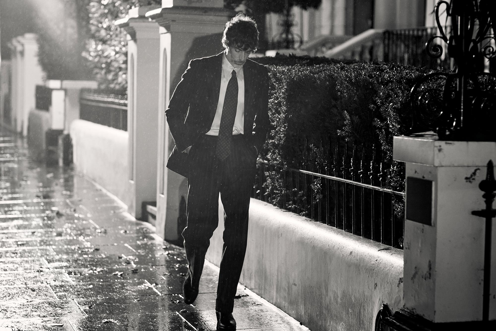 Richard walking across a wet street in a suit
